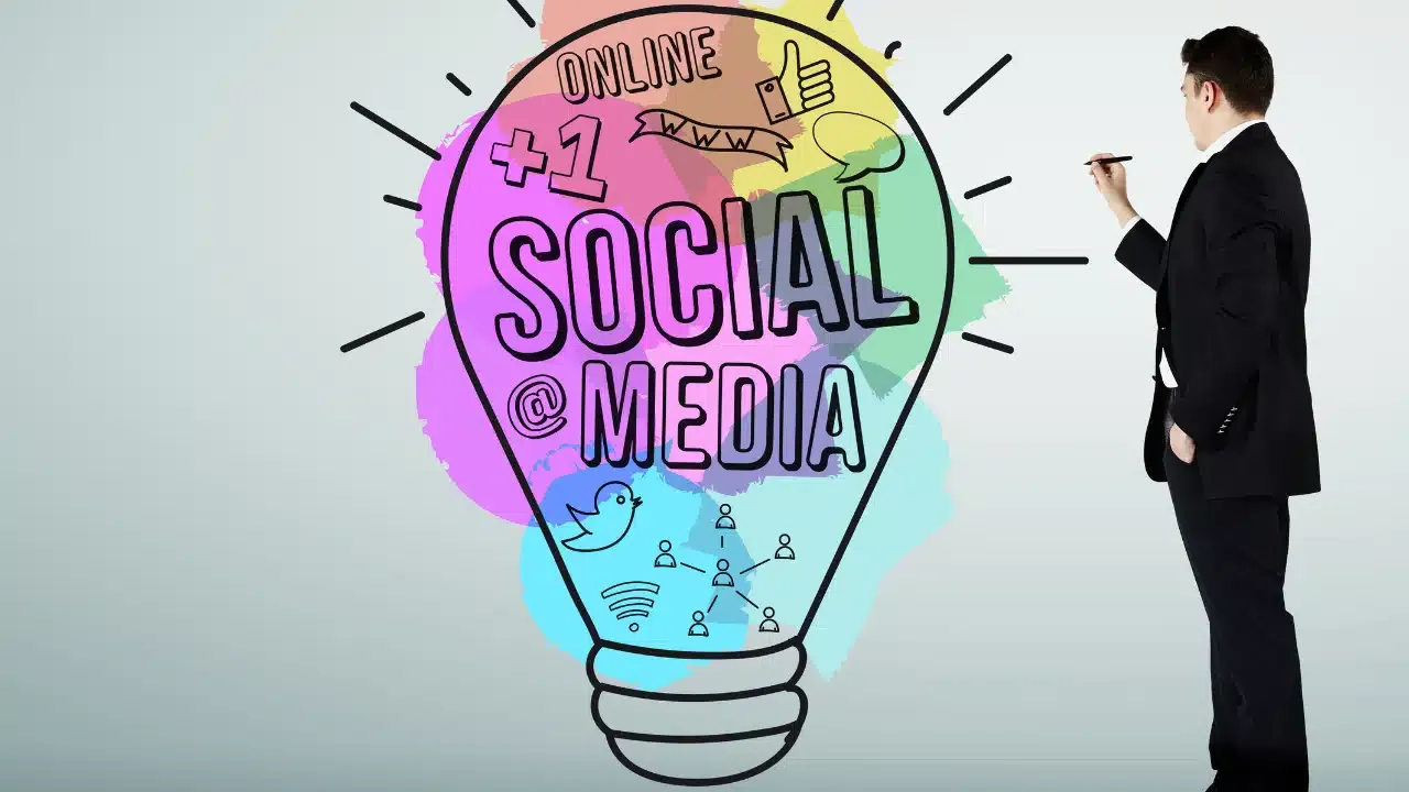 A man in a suit draws on a clear board with a colorful lightbulb illustration labeled Social Media surrounded by social media icons, including a thumbs-up, bird, and people, with the word Online at the top.