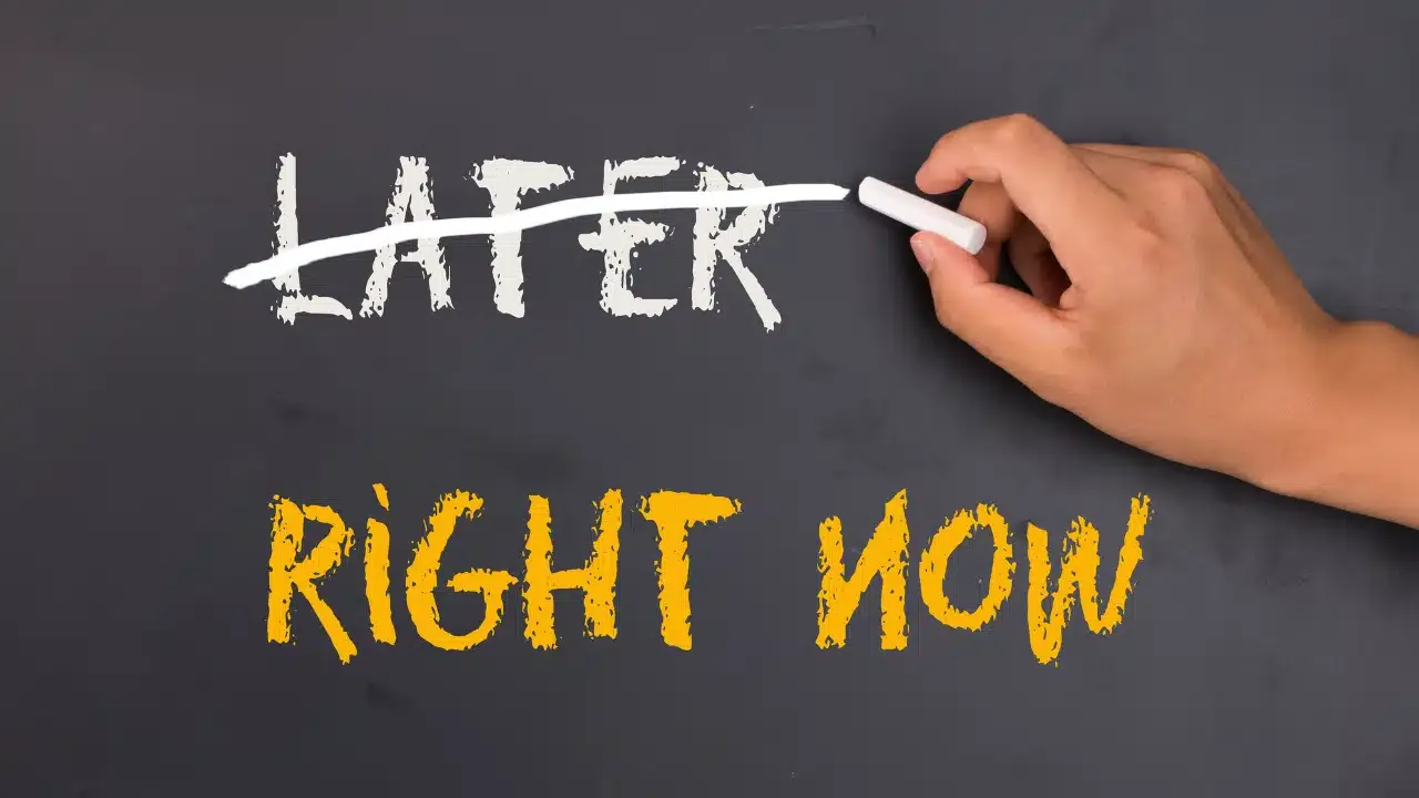 A hand with chalk crosses out the word LATER written in white on a blackboard, revealing the words RIGHT NOW in bold yellow below.