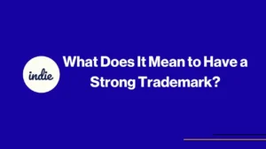 White text on a blue background reads, What Does It Mean to Have a Strong Trademark? A white circle on the left contains the word indie in script. Thin yellow and black lines appear in the lower right corner.