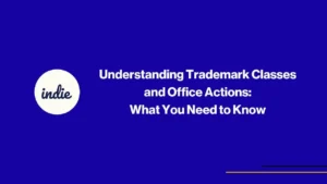Blue background with white indie logo on the left and the text Understanding Trademark Classes and Office Actions: What You Need to Know in the center. Thin yellow and blue lines at the bottom right.