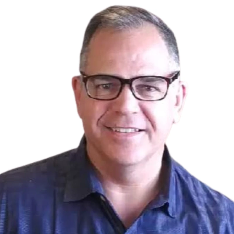 A man with short hair and dark rimmed glasses in a blue button up shirt smiles at the camera.