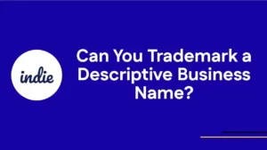 Blue background with white circle containing the word indie in script, next to bold white text reading Can You Trademark a Descriptive Business Name?. Thin yellow and white lines in bottom right corner.
