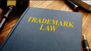 A book titled "Trademark Law" on a wooden desk beside a gavel, a pen, and a notebook.